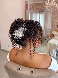 a woman sitting in front of a mirror with her hair styled into a curly updo