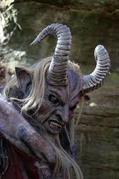 a man with long hair and horns is dressed in an evil costume, holding his arm out