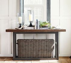 a wicker basket under a mirror on a table with candles and other items in front of it