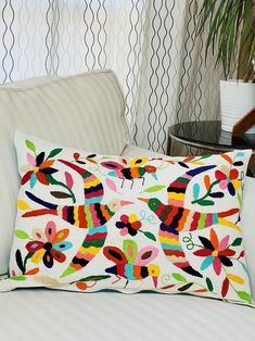 a colorful pillow on a white couch in front of a wall with black and white trellis