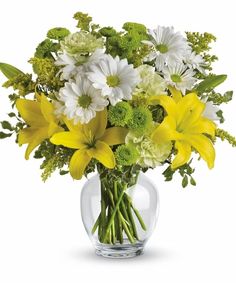 yellow and white flowers in a clear vase on a white background with greenery around it