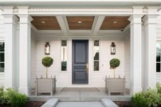 the front entrance to a white house with blue door and two planters on either side