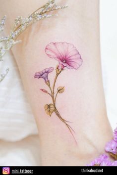 a small flower tattoo on the side of a woman's leg with purple flowers