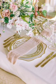 the table is set with gold and white plates, silverware, and pink flowers