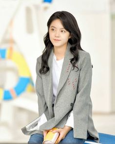 a young woman sitting on top of a blue table next to a white and yellow wall