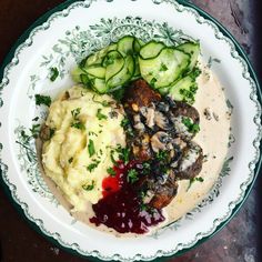 a white plate topped with mashed potatoes, cucumbers and meat on top of sauce