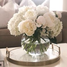 a glass vase filled with white flowers sitting on top of a table next to a couch