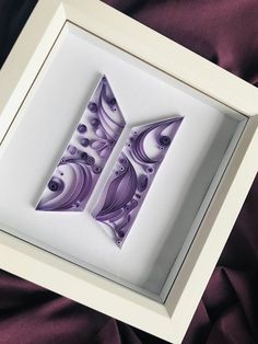 an artistic paper art piece is displayed in a white frame on a purple fabric background