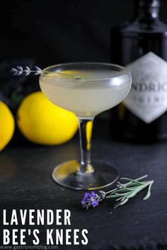 a glass filled with liquid next to lemons and lavender sprigs on a table