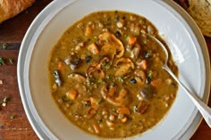 a white bowl filled with soup on top of a wooden table next to some bread