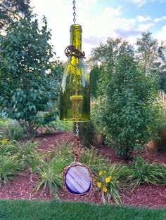 a glass bottle hanging from a chain in the grass with flowers and trees behind it