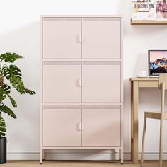 a pink cabinet sitting next to a plant in a room with white walls and wooden floors