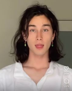 a woman with long black hair wearing green earrings and a white shirt is looking at the camera