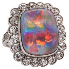 An art deco ring with Australian opal. Exceptionally beautiful ring, created during the iconic period of the art deco, back in the 1930. This colorful ring personify the deco period and has been crafted in a cushion shape in solid platinum with polished finish. The design show very strong deco patterns and is embellished with one multicolored opal gemstone. The opal has a very nice "pin fire" pattern with an unusually generous amount of blue/green/purple/red play of color. All gemstones settings are decorated with millegrain patterns. Australian Opal: Mount in the center in a bezel setting, with 1 cushion cabochon cut (14.06 x 11.70 x 4.5 mm) of a natural Australian opal of 4.36 carats, with no crazing, scratching or pitting to opal. Diamonds: Mounted around and the sides in a French flush Red Play, Colorful Ring, Opal Diamond Ring, Precious Opal, Types Of Opals, Big Rings, Jewelry Techniques, Deco Ring, Art Deco Ring