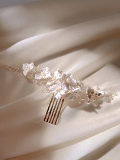 Delicate Handmade Floral Hair Comb for Brides This exquisite handmade bridal hair comb is made from from cold porcelain complemented with delicate floral accents, shimmering pearls, and crystals.  Its ethereal off-white flowers, meticulously hand-shaped, are perfect for adding a romantic, sophisticated touch to any bridal hairstyle.  The elegant sparkle from the pearls and crystals offers a luxurious finish, ideal for weddings or special occasions.  Lightweight yet elegant, this comb sits comfor Wedding Flower Comb, Pearl Hair Comb Wedding, Pearl Hair Comb, Floral Hair Comb, Pearl Hair Combs, Floral Hair Combs, Flower Comb, Floral Headpiece, Hair Comb Wedding