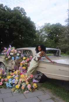 a woman leaning on the back of a car with flowers in front of her,