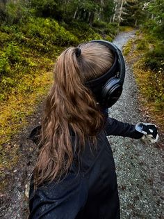 a woman with headphones on walking down a dirt road in the woods and trees