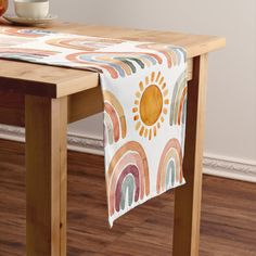 a wooden table topped with a white table cloth covered in rainbows and sun designs