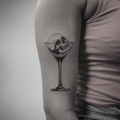 a woman with a tattoo on her arm holding a martini glass in the shape of a skull