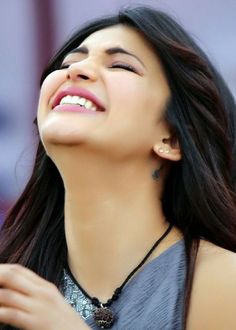 a woman is smiling and looking up at the sky with her eyes closed while wearing a necklace