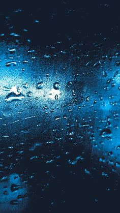 rain drops on the window with blue light behind it and dark sky in the background