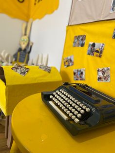 an old fashioned typewriter sitting on top of a yellow table in front of pictures