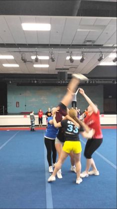 some girls are playing with a frisbee in an indoor court area while others watch