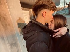 a young man and woman kissing each other in front of a building with snow on the ground