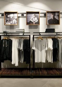 clothes on racks in a clothing store with pictures hanging from the wall and framed photos above them