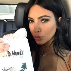 kim kardashian is posing in her car holding a bag of popcorn