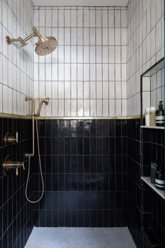 a black tiled shower with brass fixtures and hand held shower head in the corner next to shelves