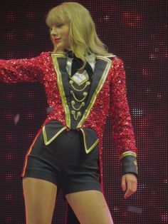 taylor swift performing on stage at an event wearing a red and black outfit with gold trimmings