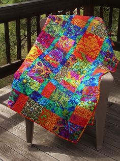 a multicolored patchwork quilt sitting on top of a wooden deck next to a chair