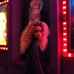 a woman with long blonde hair standing in front of a mirror and lights on the wall