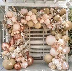 an arch made out of balloons with flowers and leaves on the top is decorated in gold, pink and white