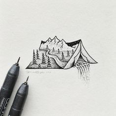 two pens are sitting on top of a piece of paper with a drawing of mountains and trees