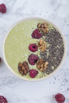 a bowl filled with green smoothie topped with nuts and raspberries