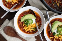 three bowls filled with chili and topped with avocado