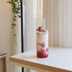 a white table topped with a red drink next to a window