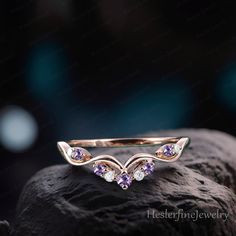 a gold ring with purple and white stones on top of a black rock in front of a blurry background