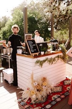 a man and woman standing at a counter in front of a bar with plants on it