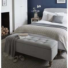 a bedroom with blue walls, white bedding and gray footstools on the floor