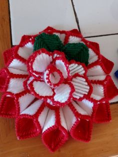 a red and white crocheted flower sitting on top of a wooden floor next to a tile wall