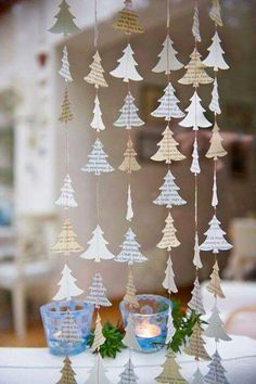 paper christmas trees hanging from the ceiling in front of a table with two cups on it