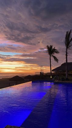 an empty swimming pool at sunset with palm trees in the background and lights shining on the water