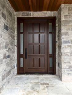 the front door is made of wood and has glass panels on each side, along with stone walls