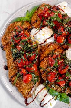 a white plate topped with meat patties covered in tomatoes and spinach leafy garnish