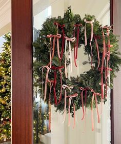 a wreath hanging on the front door of a house decorated for christmas with ribbons and bows