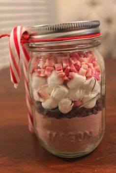 a mason jar filled with marshmallows and candy cane on top of a wooden table