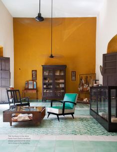 a living room filled with furniture next to a tall yellow wall and wooden shelves on either side